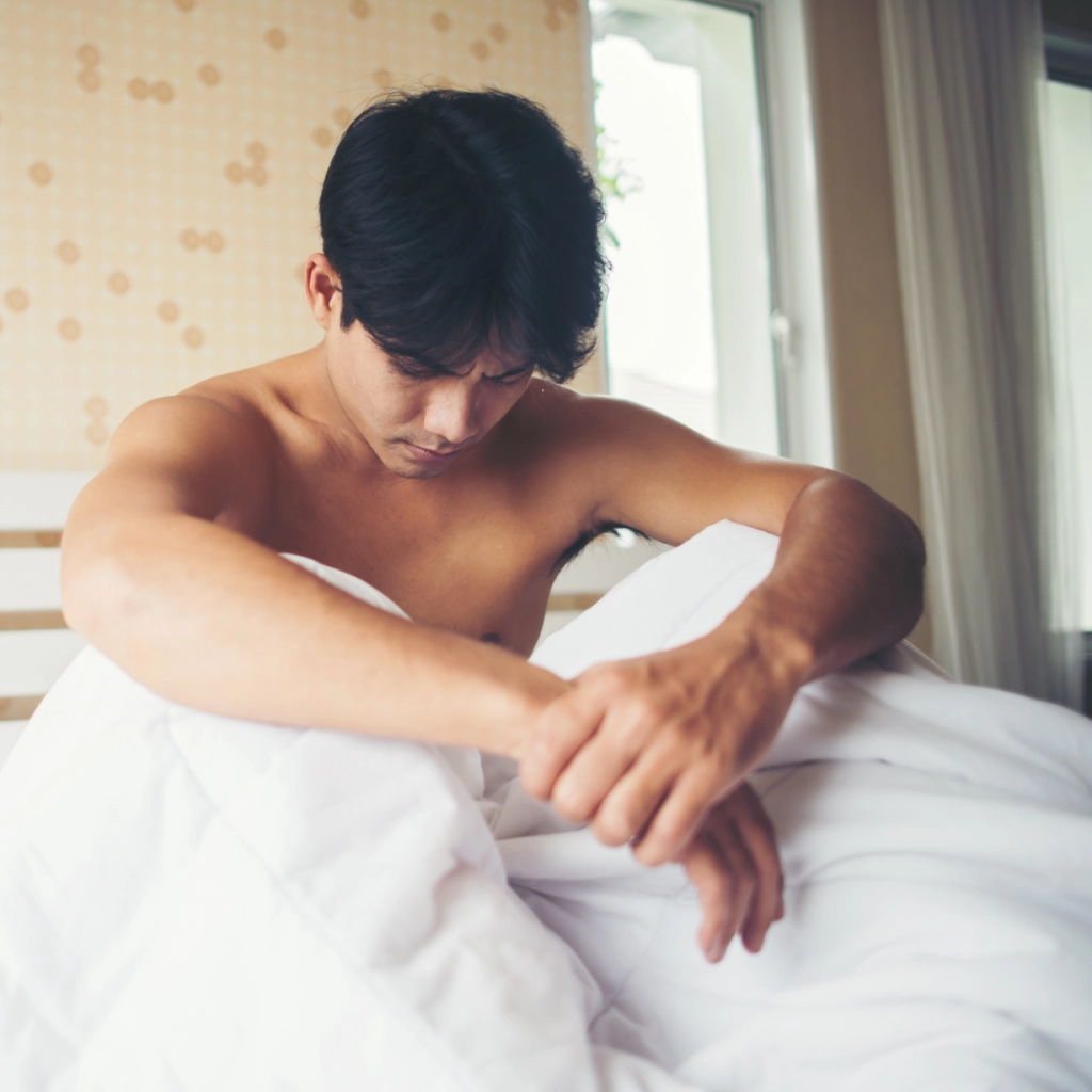 Hombre sentado en la cama con malestar relacionado con dolor pélvico o disfunción sexual
