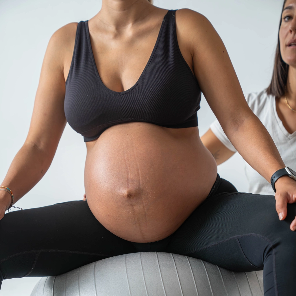 Mujer embarazada realizando ejercicios sobre fitball acompañada por fisioterapeuta