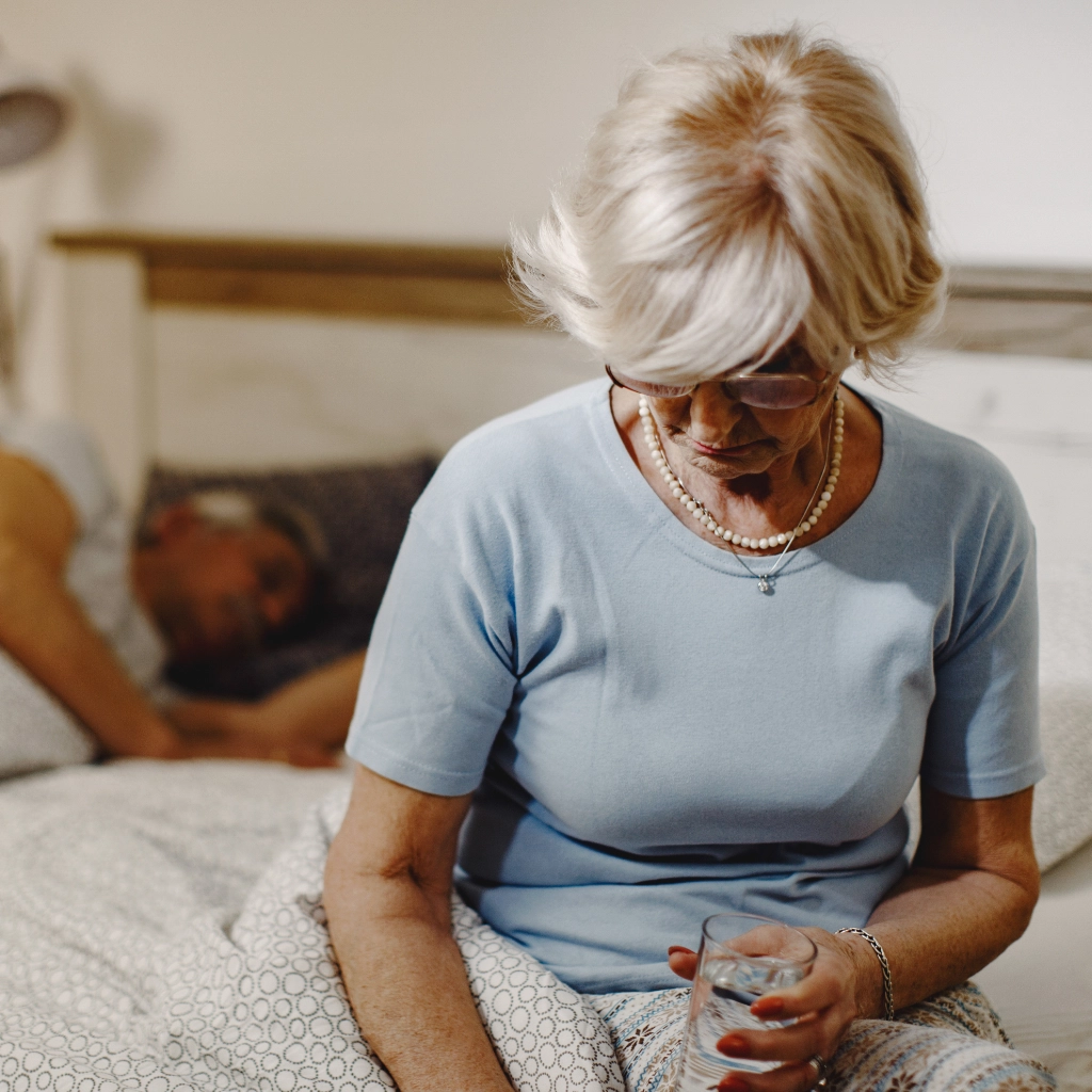 Mujer en menopausia sentada en la cama con molestias nocturnas relacionadas con el suelo pélvico